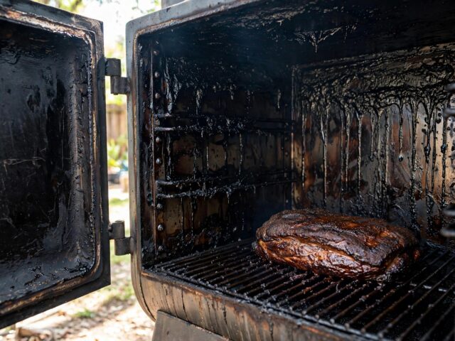 Open smoker with black tar-like creosote coating the interior walls and a brisket on the grate