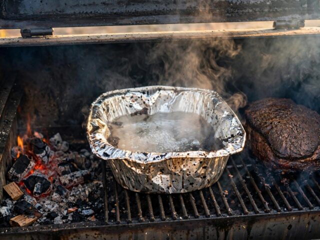 Steaming water pan in an offset smoker beside a brisket with dark bark
